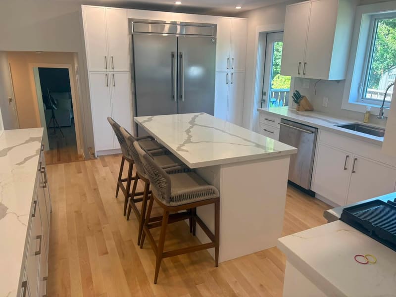 Long quartz island with woven bar stools in an open-plan kitchen